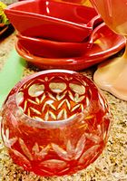 Red patterned faceted glass candle holder and red ceramic dishes stacked behind