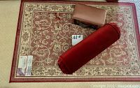 Small rectangular rug with red and cream floral patterns with a round red pillow and brown electric shoe shine device on top.