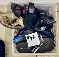Top view showing six pairs of men's slip-on shoes and thong sandals in mixed colors and materials in a plastic bin, with a note '#46'.