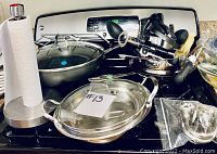 Overview photo of silver tone kitchenware on a stove including pans, glass bowls, a paper towel stand, and various metal kitchen tools.