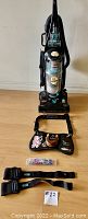 Front view of Bissell upright vacuum cleaner with weight belts and fishing accessories arranged on floor.