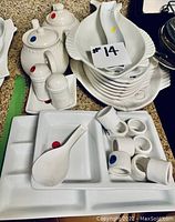 White ceramic kitchenware including fish-shaped serving plates stacked together, two teapots with lids, salt and pepper shakers, napkin rings, white divided tray, and ceramic spoon.