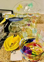 Yellow glassware including leaf-shaped bowls, colorful small glasses, clear container, knives and utensils with yellow handles, wooden corn holders, decorative cheese platter