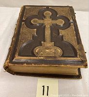 Bible closed on its back, showing dark brown leather cover with embossed gilt cross and decorative tooling
