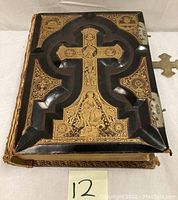 Front cover showing black leather cover with gold embossed cross and tooling, brass clasp and corner hardware