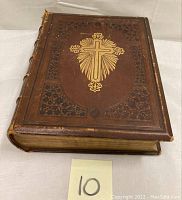 Front cover of an antique Holy Bible with brown leather binding, embossed cross and ornate detailing.