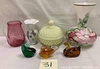 Overview of the lot showing all items including Fenton yellow satin custard hobnail covered bowl, pitchers, vases and glass paperweights.