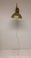 Full view of the brass wall hanging lamp mounted on wall showing curved arm, wooden base, and hanging dome shade with electric cord.