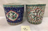 Pair of Chinese ceramic planters decorated with famille rose enamel. Both planters are round with vibrant blue backgrounds, turquoise rims, and floral medallions.