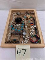Full view of the wooden tray holding assorted costume jewelry items including bracelets, earrings, brooches, pendants, necklaces, and two wristwatches.