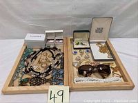 Full view of two wooden trays holding assorted costume jewelry including necklaces, bracelets, Pandora boxes, and a pair of sunglasses.