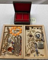 Open black jewelry box with red velvet interior and compartments, showing the collection of costume jewelry inside wooden trays.