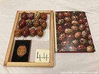 Photo showing the 16 lacquered wooden eggs arranged on a wooden tray (not included) alongside the Russian Cooking cookbook with a cover displaying traditional decorated eggs.