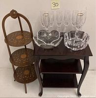 Full lot including marquetry pie stand on the left, dark wood end table on the right, six crystal champagne flutes with gold rims on the table, and two Orrefors crystal bowls in front.