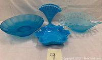 Photo showing four blue glass bowls with reticulated and ruffled edges in different shapes and frosted finishes.