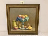 Framed oil on canvas still life painting with fruit and ceramic containers on a table.