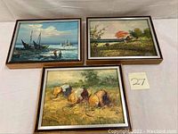 Three framed oil paintings arranged side by side on a white surface, showing nautical, countryside and harvesting scenes