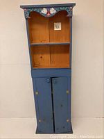 Full view of the painted narrow wooden hutch showing upper shelves and lower doors with floral design on the top edge