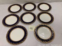 Overview of nine matching porcelain plates arranged on a flat surface, showing the dark blue and gold gilt floral decoration and white centers.