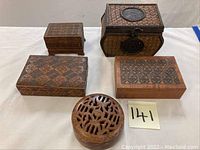 Five wooden boxes displayed on a white surface, varying shapes including round and rectangular with carved designs