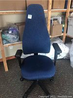 Front view of blue upholstered high back office chair with black arm rests and wheeled base.