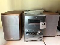 Full system includes central DVD component with control knobs and buttons, two speakers, and a remote on top of unit.