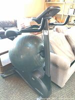 Side view of the stationary fitness bike showing the seat, handlebars, and attached exercise ball behind the bike.