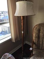 Full view of the floor lamp showing wood turned base and fabric shade with tear.
