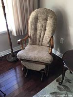 Front view of oak glider rocker chair with beige-green damask patterned upholstered seat and back