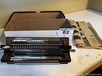 Front view of six stacked harmonicas mounted in rotating frame next to storage box and booklet.