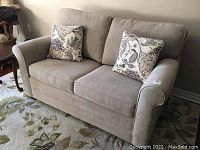 Front view of beige loveseat sofa bed with two floral throw cushions on area rug