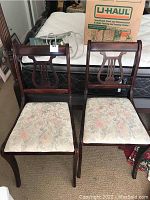 Two matching wooden chairs with lyre-shaped backs and floral upholstered seats side by side.
