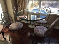Dining table and four matching chairs with floral cushions in front of window.