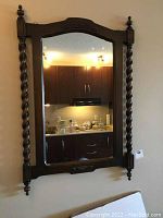 Full front view of the wall mirror showing the carved dark wood spool-turned side columns and finials, reflecting kitchen cabinets.