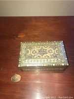 Photo of a decorated rectangular jewelry box with star patterns and a small 9ct gold pendant on a wooden surface.