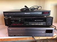 Front view of the three stacked devices: Panasonic DVD/CD player on top, Akai VHS stereo receiver in the middle, Yamaha CD changer at the bottom, showing all controls and displays.