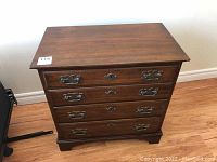 Front view of the wooden four-drawer nightstand showing the metal handles and general wear.