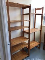The shelving unit assembled showing six pine wooden shelves on two adjoining vertical frame sections, highlighting the natural pine wood color and minor stains on shelves.