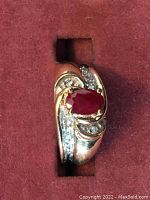 Top-down view of ring showing oval ruby and diamond accents against red background.