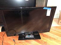 Front view of the Ario LED TV sitting on a black stand, displaying the screen and the remote control placed on the stand base.