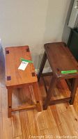 Two wooden bar stools side by side on wood floor, one light and one dark wood, damaged and showing wear