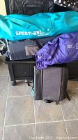 Photo of teal blue Sport-Brella beach chair bag and purple folding chair bag placed together with black foldable seat/cushion on tiled floor.