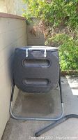 View of front of black plastic compost bin on metal stand, showing large horizontal indented ventilation areas.