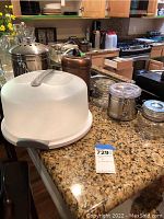 Wide view of decorative jars, glass bottles, and containers on granite kitchen counter showing various metal and glass kitchenware items.