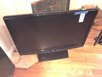 Photo of front view of the JVC flat-screen LED TV showing screen, bezel and stand, with a small white label on top right corner.