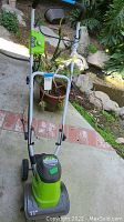 Full view of the Greenworks lawn tiller showing upright handle and tiller base outdoors.
