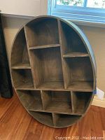 Front view of the oval wooden shelf showing multiple compartments.