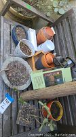 Overview photo of assorted pots including terracotta, plastic, and ceramic. Some pots contain soil and plants. Also includes outdoor lighting fixtures.
