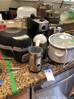 Wide view of all kitchen appliances on countertop showing T-Fal air fryer, espresso maker, kettle, coffee grinder, slow cooker, and metal container.