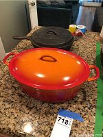 Black Texsport cast iron Dutch oven with lid, placed behind a bright orange enameled Dutch oven on a granite countertop.